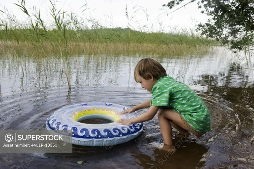 Boy playing with inner tube at edge of lake