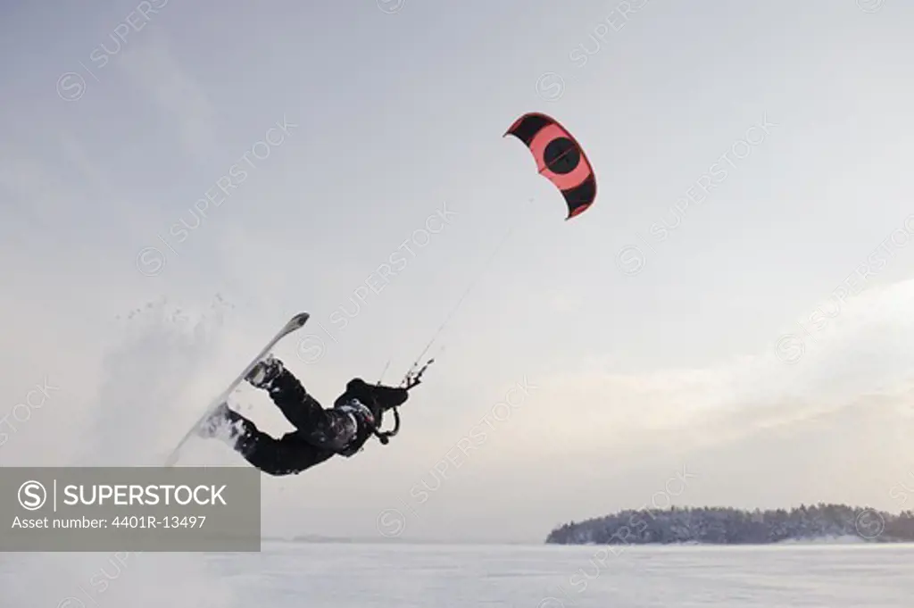 Man jumping in mid air while kiteboarding in snow