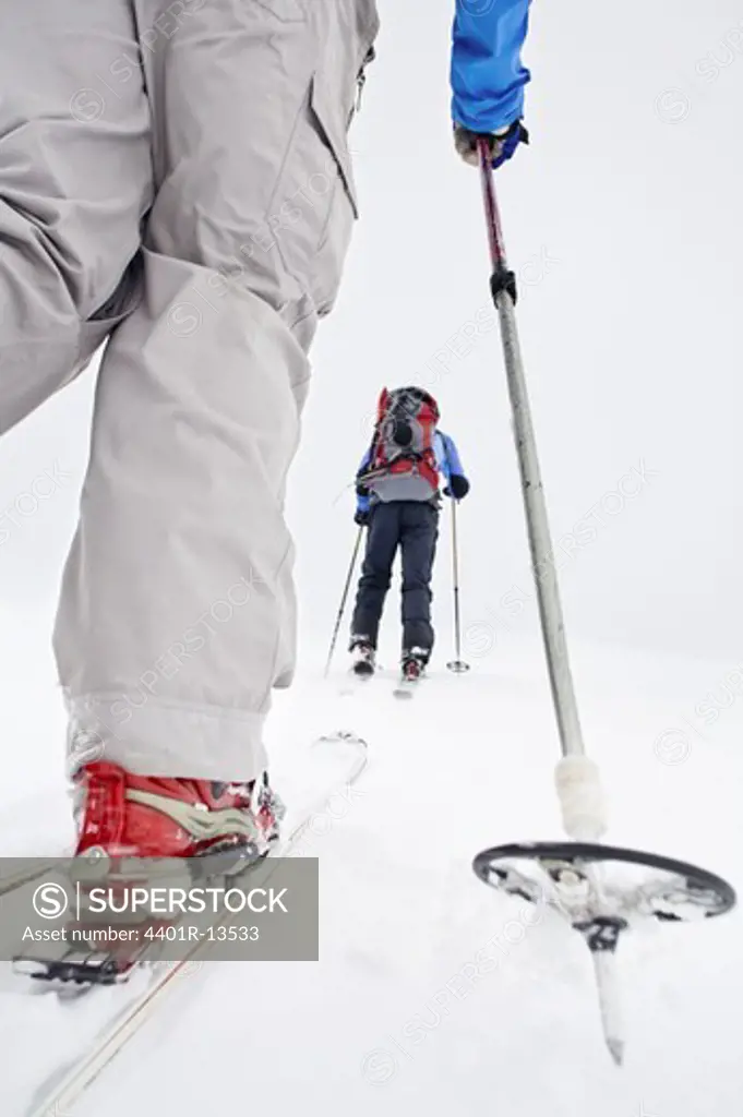 Two people walking on snow with ski and ski pole