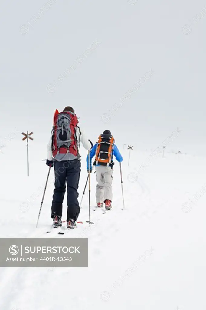 Two people carrying rucksacks walking on snow