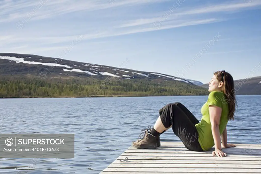 Young woman sitting on pier in lake