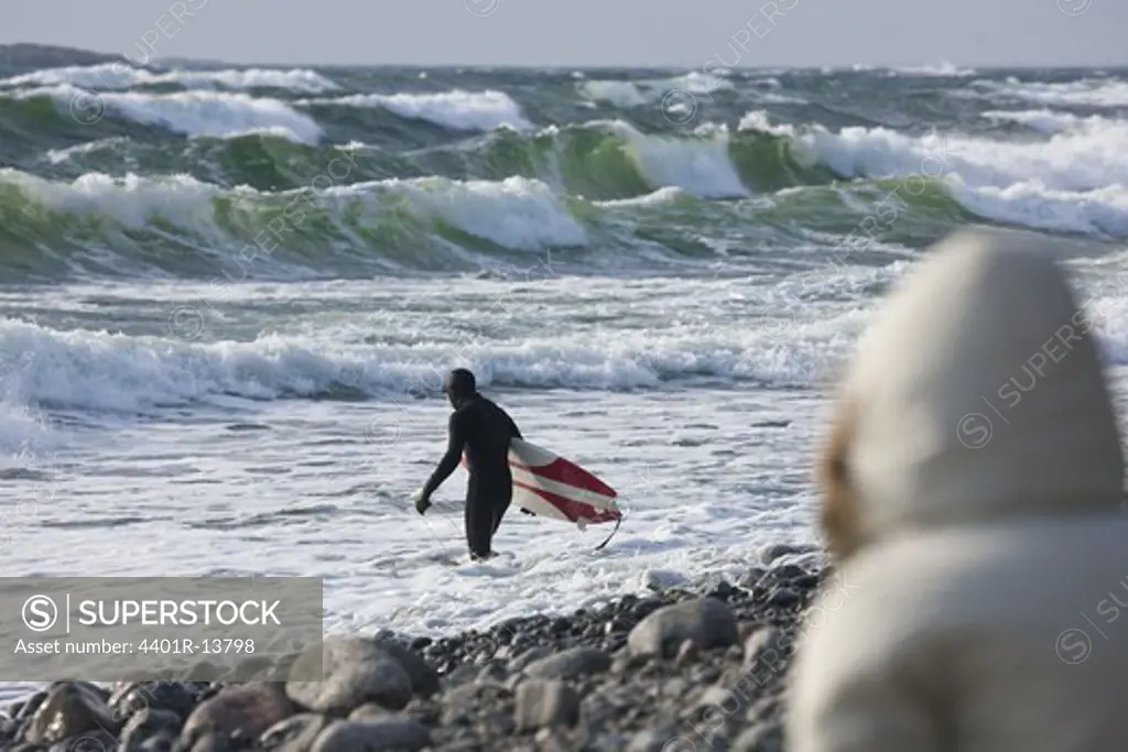 Surfer carrying surfboard in wavy sea