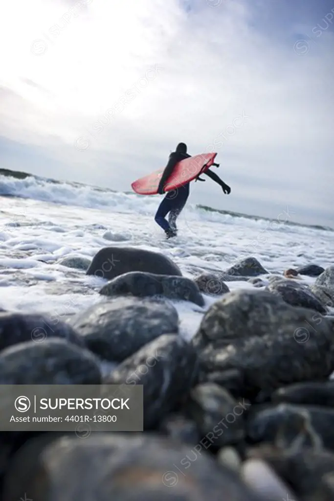 Surfer carrying surfboard into sea