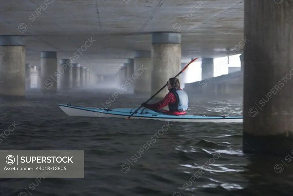 Man paddling in kayak under bridge