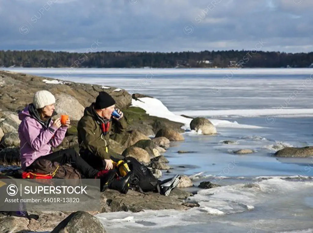 Young couple drinking coffee on rocks by sea