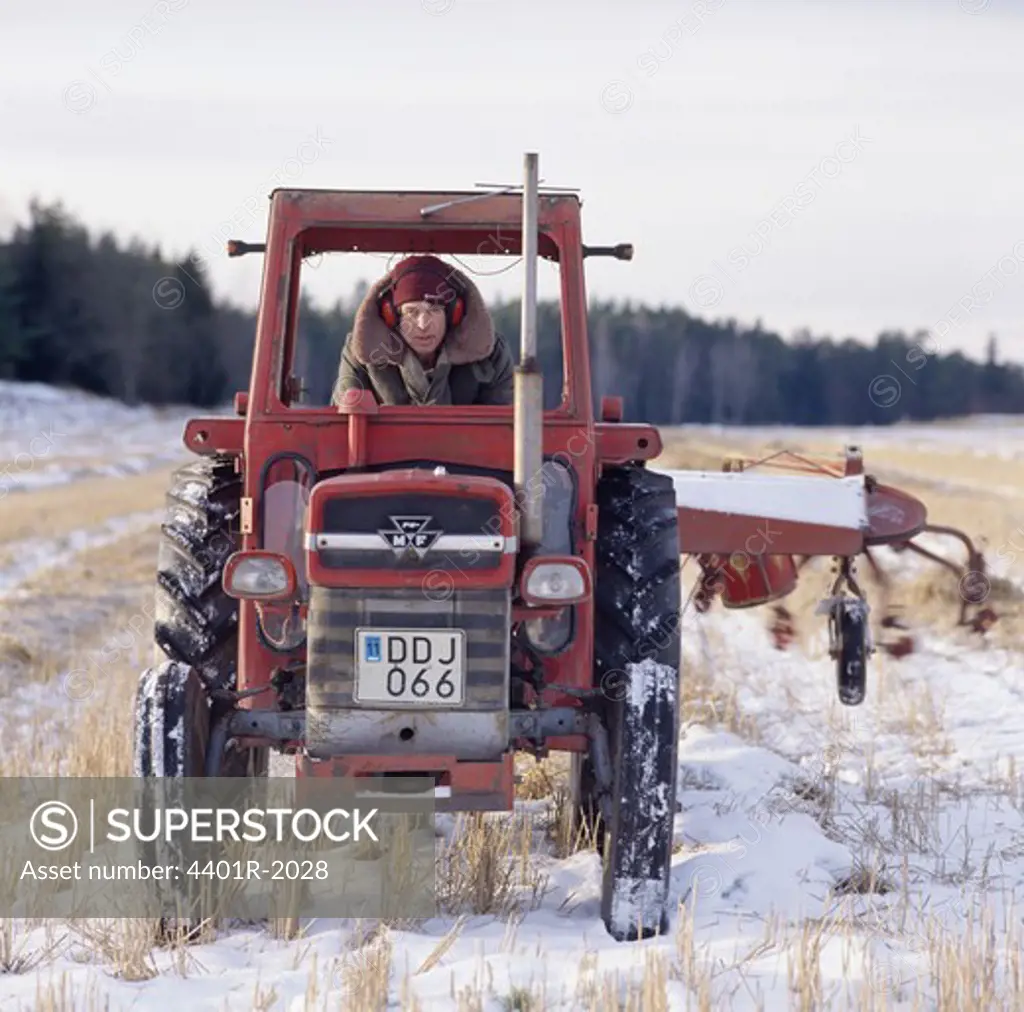 Young man driving tractor in snow-covered field