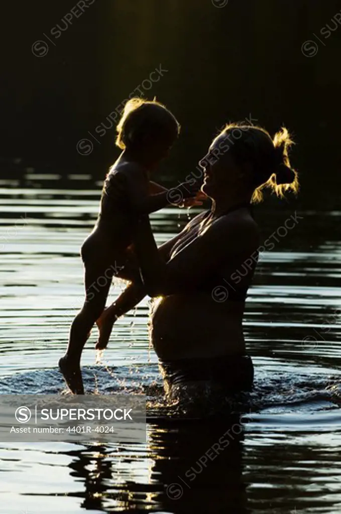 Pregnant woman playing with her child standing in the water, Ostergotland, Sweden.