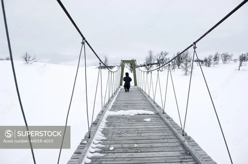 A child crossing a suspension bridge in the winter, Sweden.