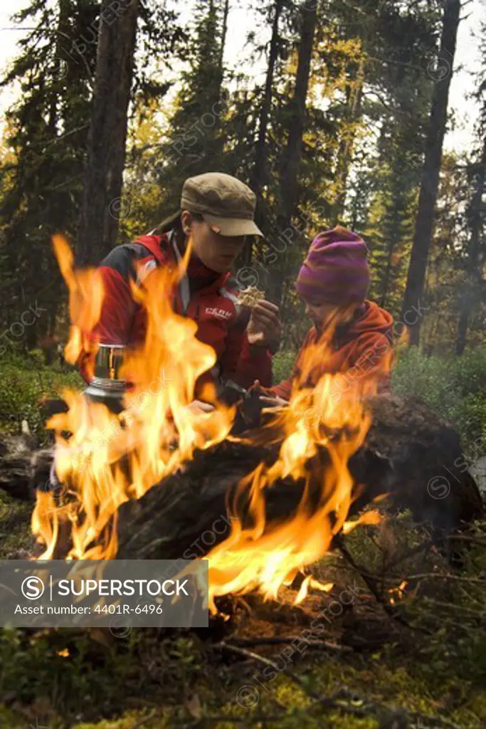 A woman and a child by a camp fire in a forest, Sweden.