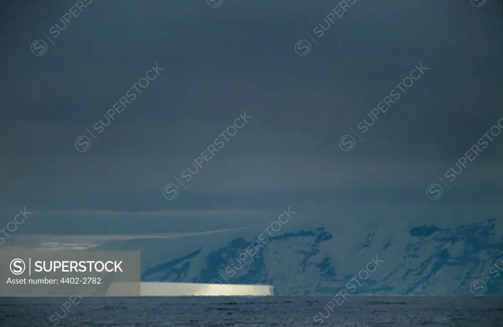 Stormy sky showing iceberg lit up by a shaft of sunlight,  Antarctica