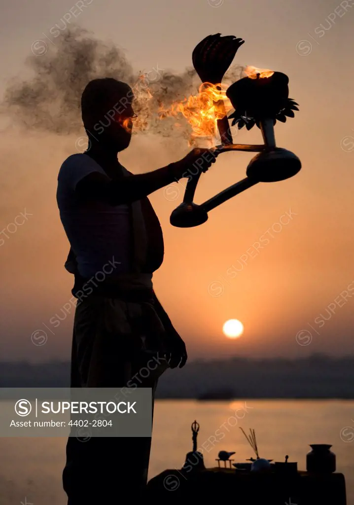Hindu holy man performing a religious ceremony (puja) to celebrate sunrise on the banks of the Ganges, Varanasi, India