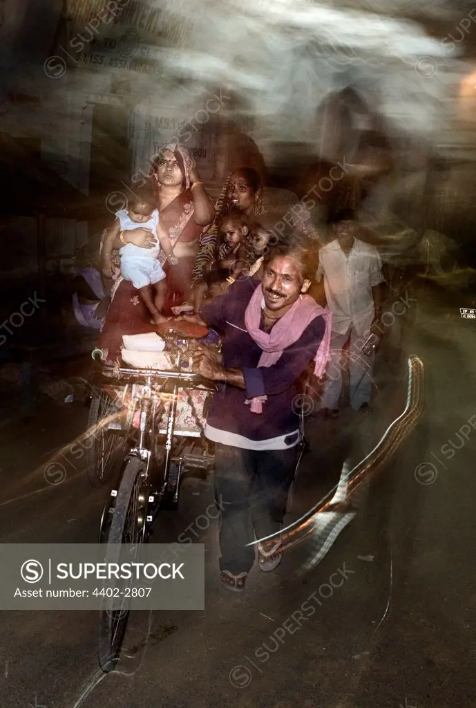 Family travelling on bicycle rickshaw at night, Varanasi, India