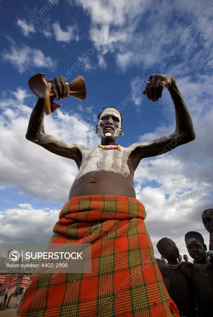 Karo tribesman with white clay body decoration, dancing while holding his traditional wooden stool, Omo Delta, Ethiopia, Africa.