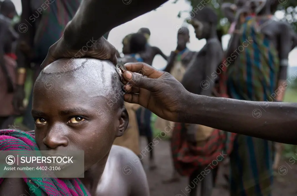 Boy of the Suri Tribe having his head shaved, Omo Delta, Ethiopia.