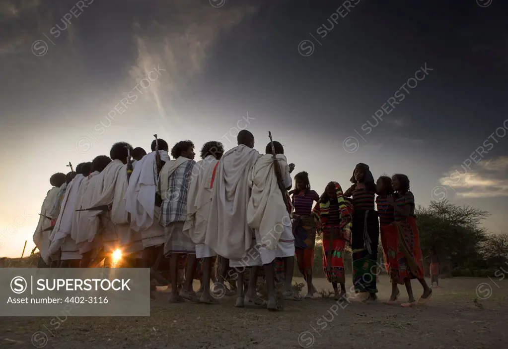 Men, wearing white, dancing with a group of young women, Afar tribe, Ethiopia