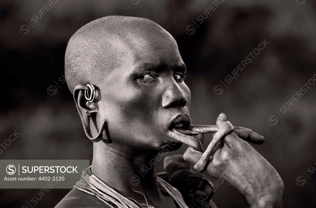 Suri tribeswoman playing with lip stretched to take a lip plate, Omo Delta, Ethiopia