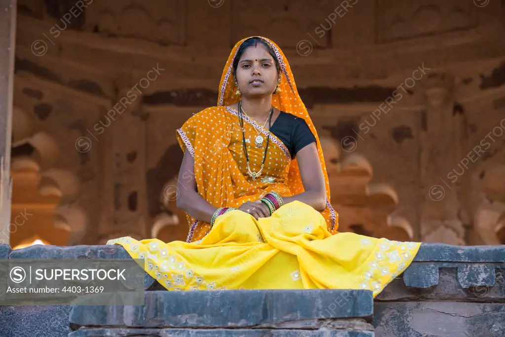 Rajasthani Woman in traditional dress sitting in sunlit opening on steps of old building Ranthambhore Rajasthan India
