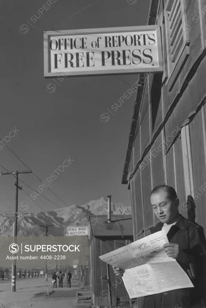 Roy Takeno reading paper in front of office, Ansel Adams