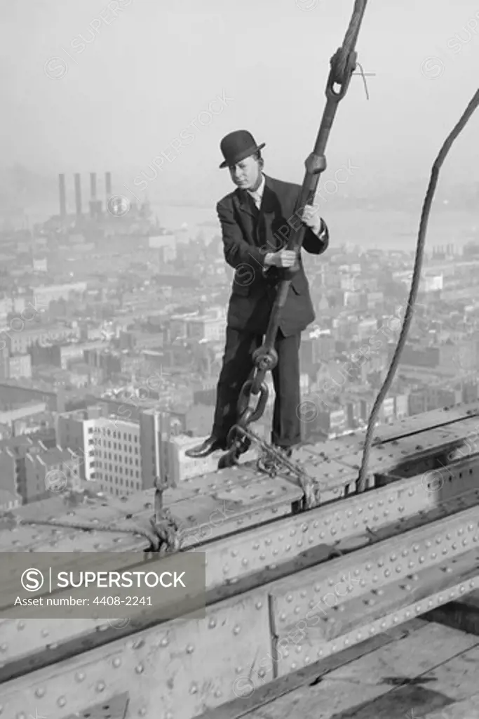 Cameraman in suit holds onto cable as he walks unharnessed over a skyscraper's steel girders, Construction
