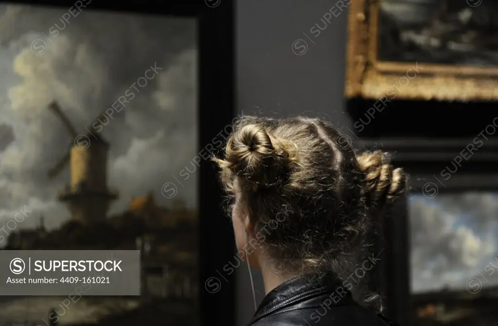 Holland. Amsterdam. Rijksmuseum. Young woman looking a Jacob Isaackz van Ruisdael (c. 1628-1682) painting The Windmill at Wijk bij Duurstede, c. 1668-1670.