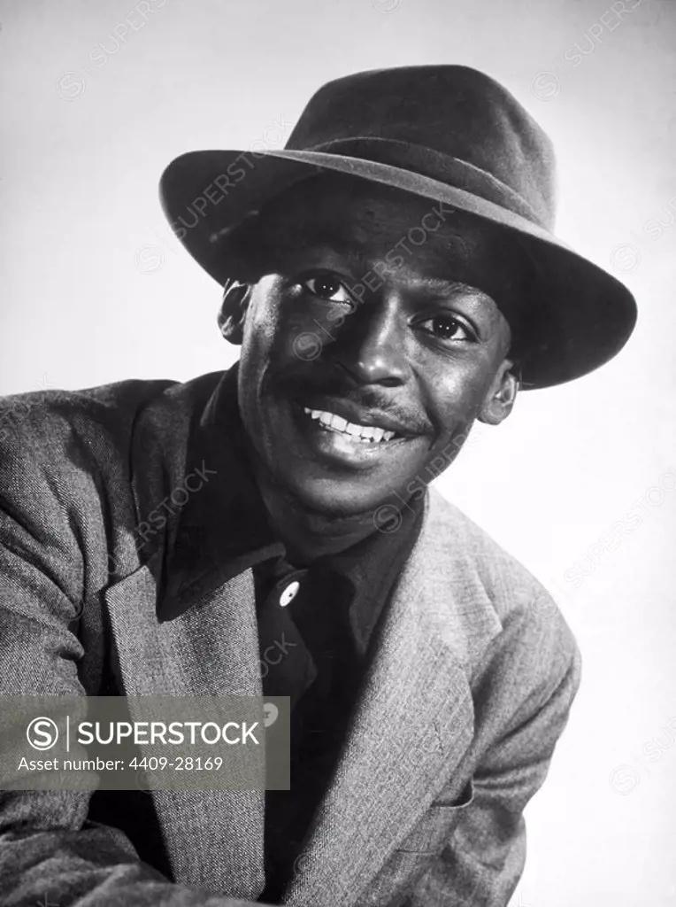 Portrait of American jazz trumpeter and banleader Miles Davis smiling and wearin a hat, whith a blazer and a dark shirt. 1947.