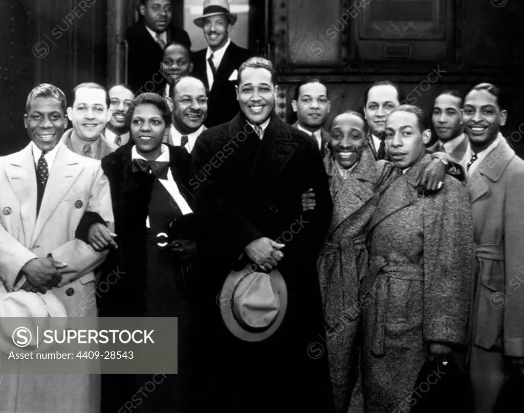 Group portrait of American jazz musician Duke Ellington and his band wearing in overcoats in front of a train, Los Angeles, California. Among those picture are: Harry Carney (far left), Sonny Greer (far right) and Ivie Anderson nex to the Duke. 1934.