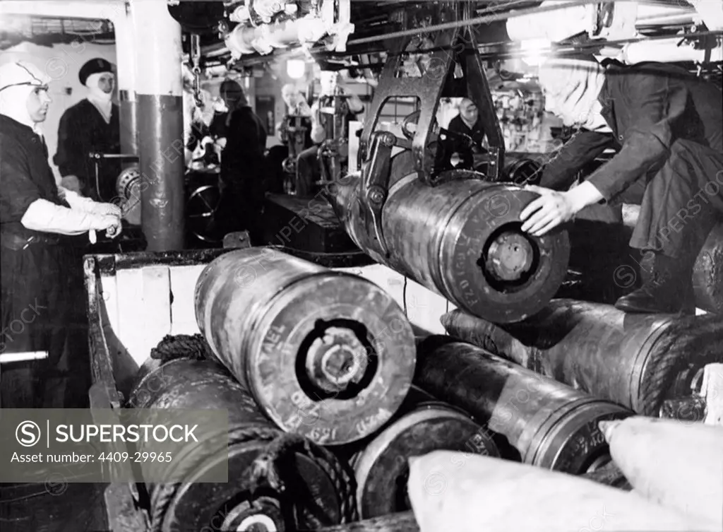 In the shell room of a battleship of the Queen Elizabeth class, 15" projectiles being handled by a mechanical grip.