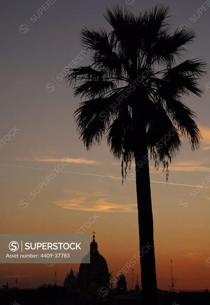 Italy. Rome. Sant'Ambrogio e Carlo al Corso, usually known as San Carlo al Corso with the dome of St. Peter's Basilica in the background, at sunset. Backlighting.