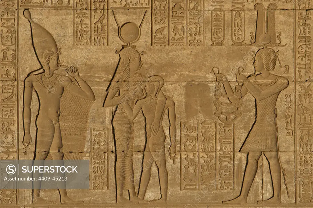 Egypt. Dendera. Temple complex. Roman Birth House of Mammisi. The Roman Emperor Trajan, depicted as a pharaoh and wearing a shuty crown, offers a necklace to the goddess Hathor while she is suckling her son, the god Ihy, who is represented as adult, on the left, with white crown or hedjet. Relief.