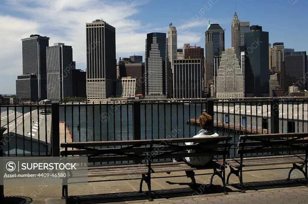 Woman sitting on a bench in Brooklyn Heights Promenade watching the Manhattan skyline. New York. United States.