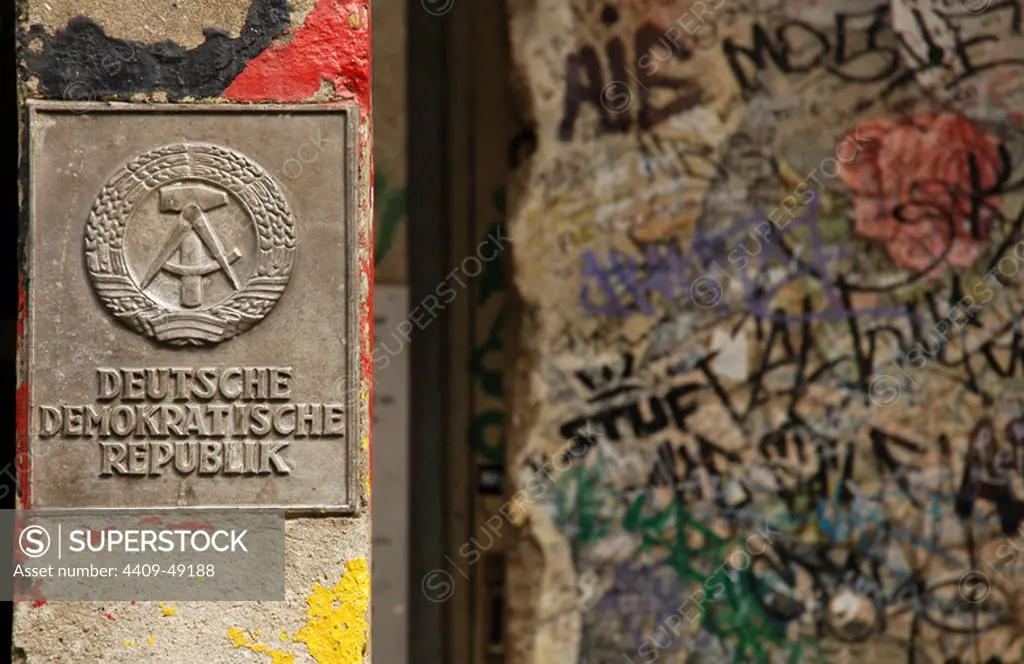 Germany. Berlin. The National Emblem of the German Democratic Republic. A hammer and a compass, surrounded by a ring of rye next to a section of the Berlin Wall.