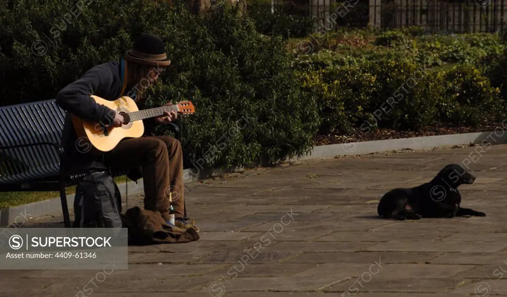 Street musician playing the guitar sitting on a bench. London. England. UK.
