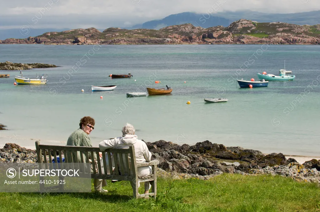 Elderly people sitting on bench at beach front, Isle of Iona, Inner Hebrides, Scotland