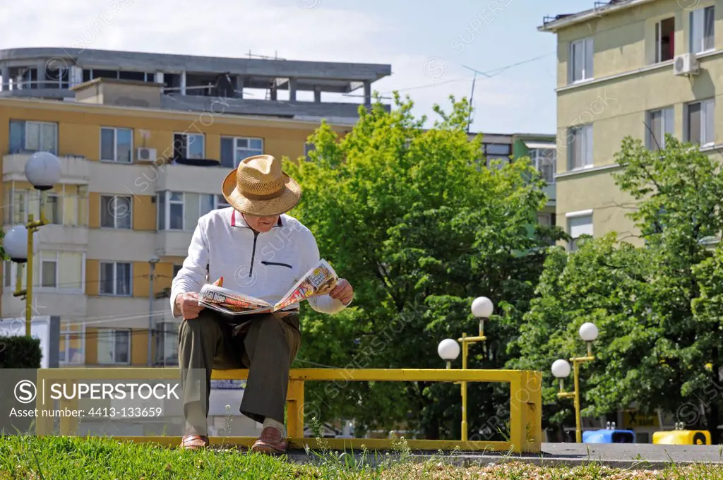 Man reading a newspaper on a bench in a city Romania
