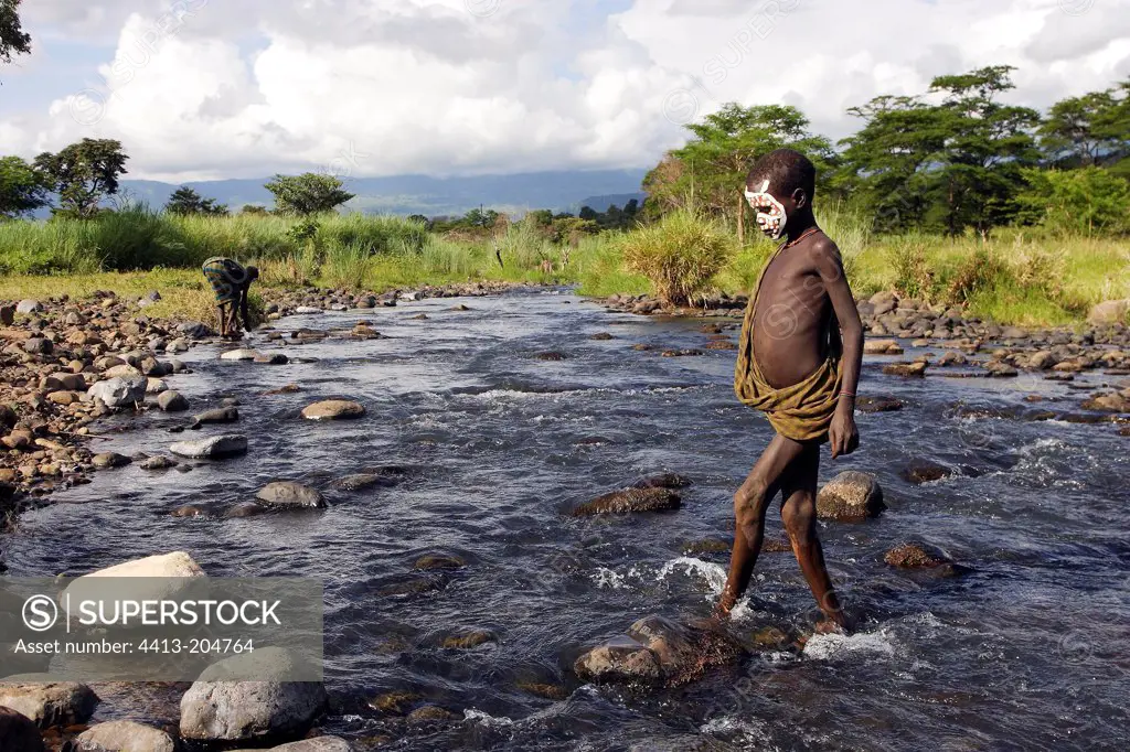 Surma boy with face paintings crossing a river Ethiopia