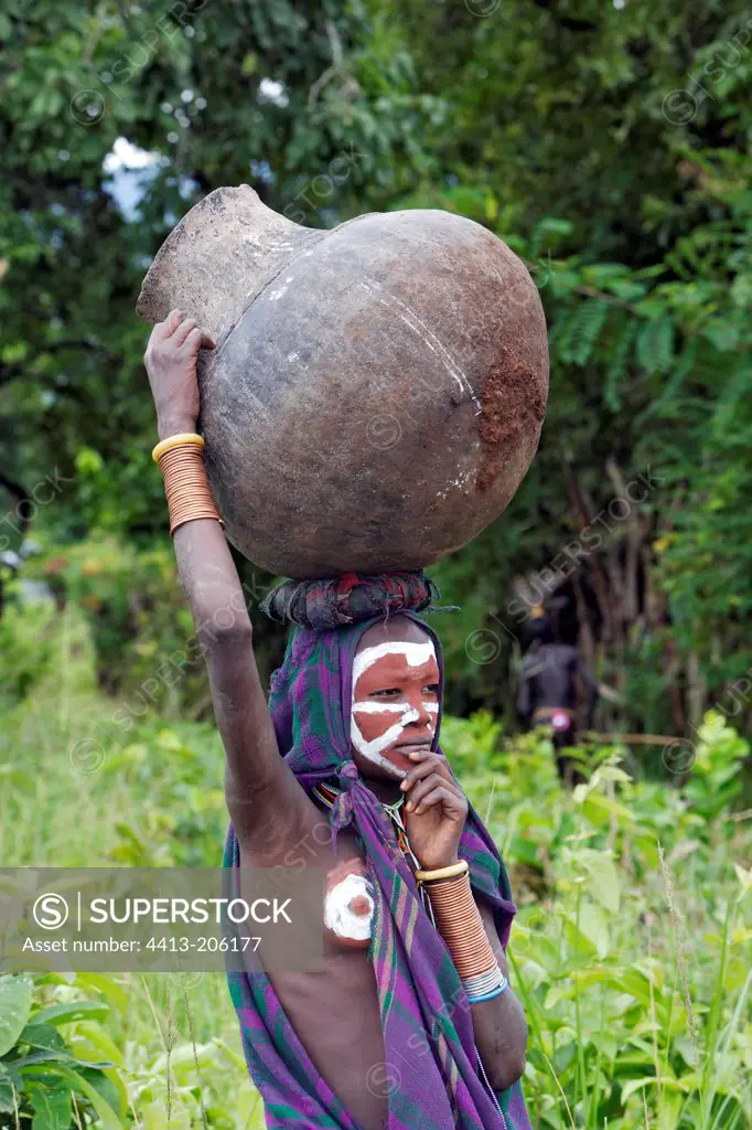 Body-painted Surma teen girl carrying a big jar Ethiopia