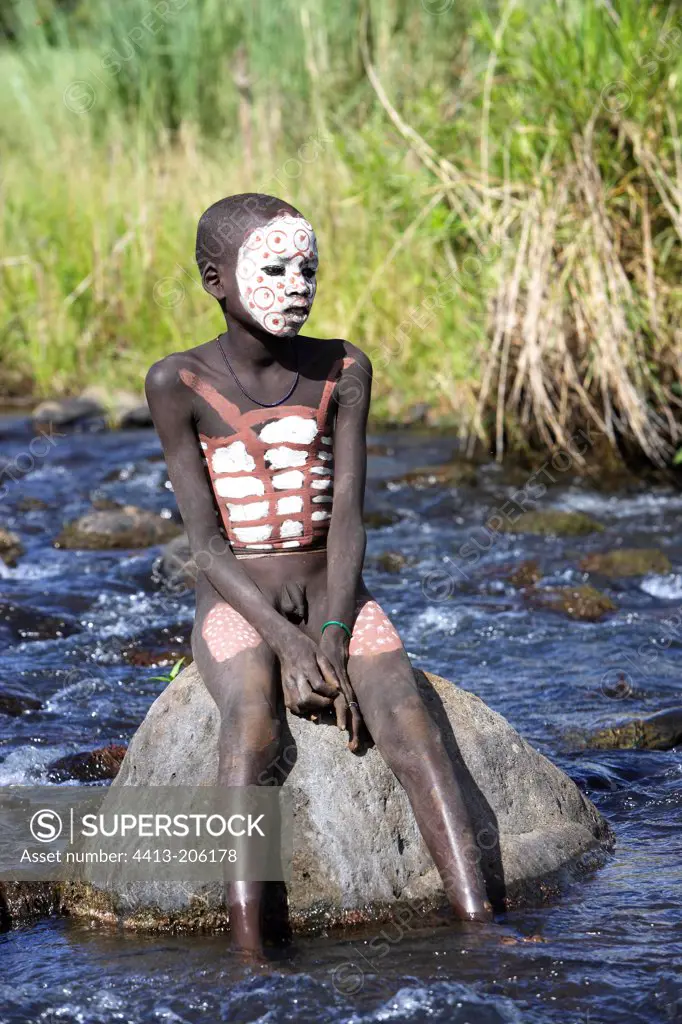 Body-painted Surma boy sitting on a rock in a river Ethiopia