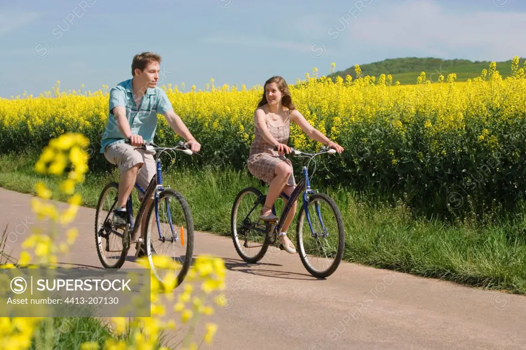 Young people walking by bicycle in the middle of Rapeseed