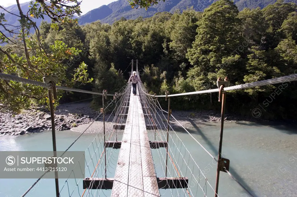 Tourist crossing wire suspension bridge over Haast River