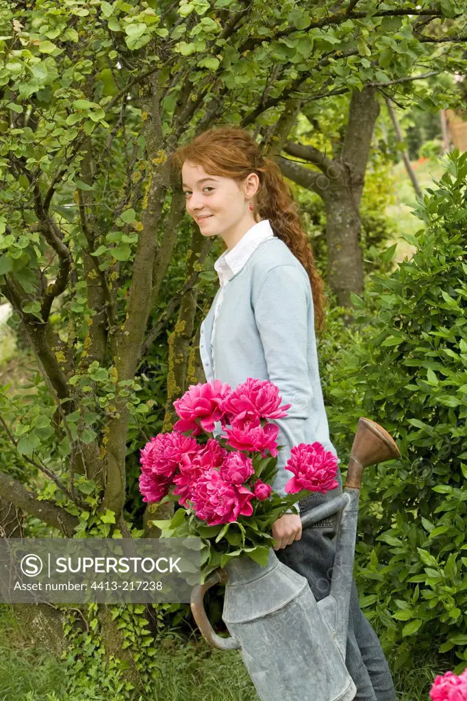 Young girl carrying herbaceous peonies in a watering can