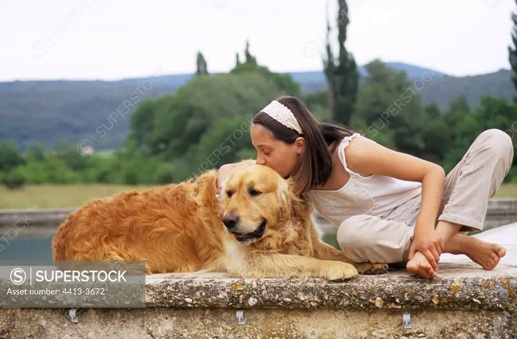 Young girl cuddling a Golden Retriever on a low wall France