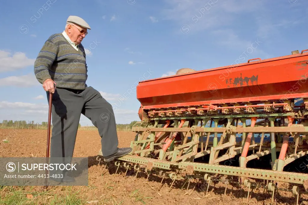 Retired farmer looking at a sowing machine in a field France