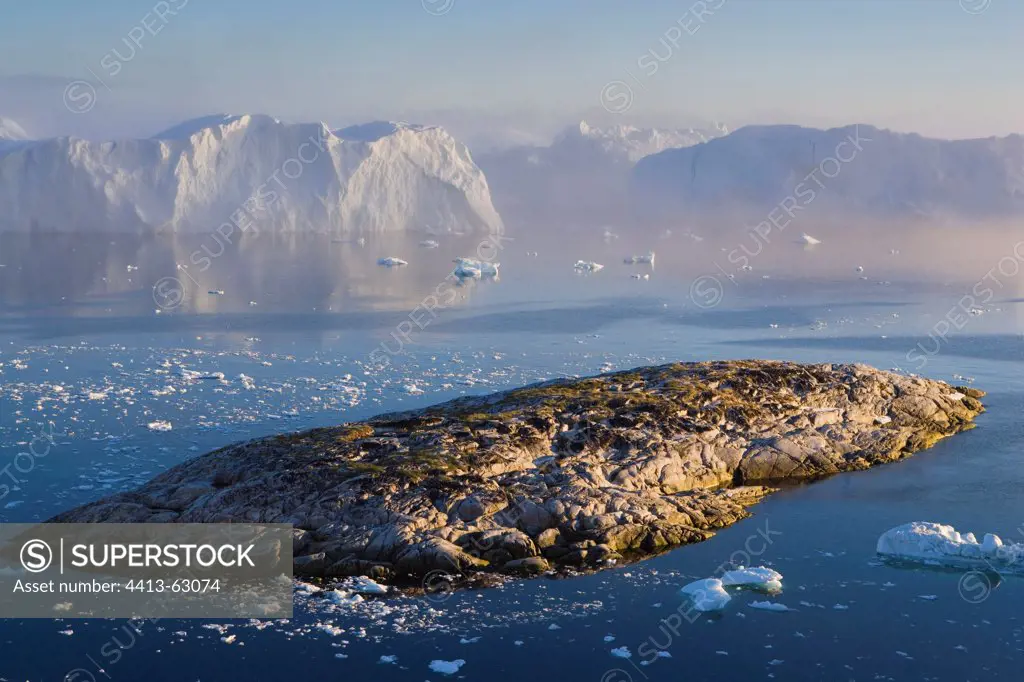 Rocky island and large icebergs at midnight Greenland