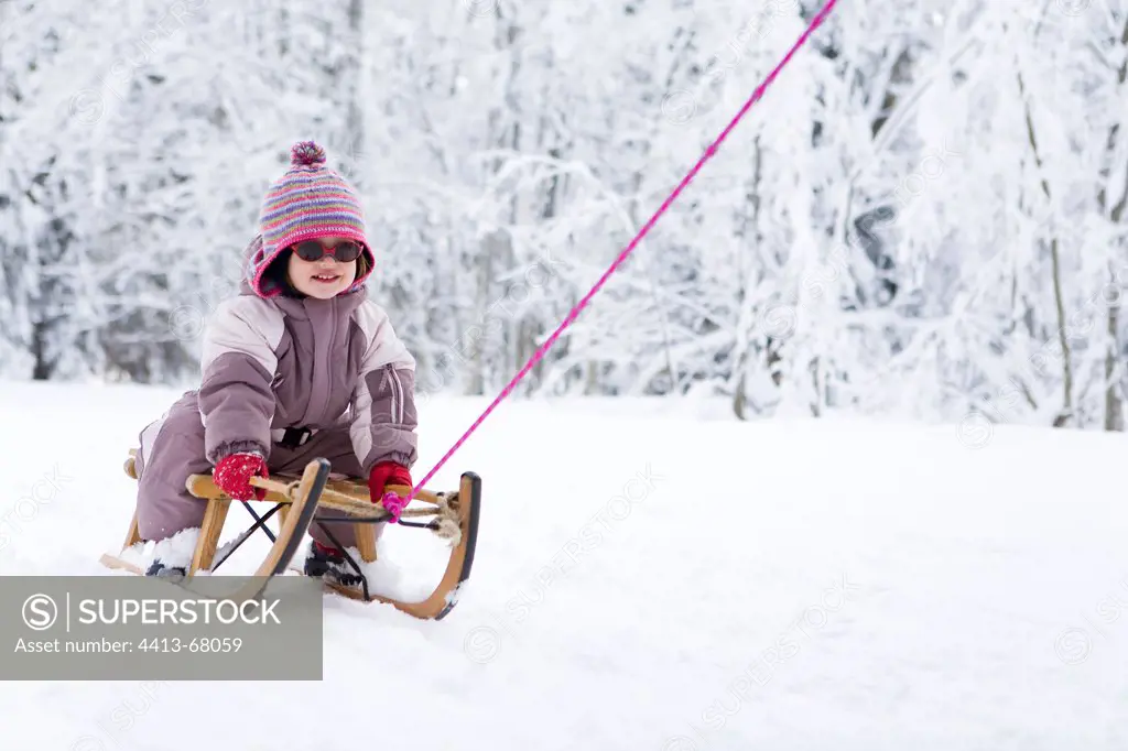 Little girl on a wooden sledge on a snowy runway