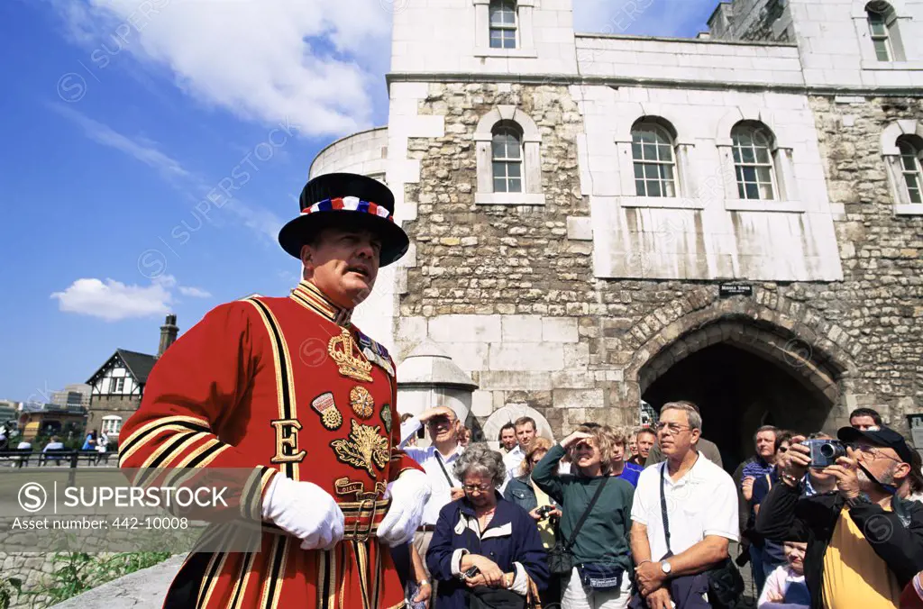 Group of people with a beefeater standing in front of a building, Tower of London, London, England
