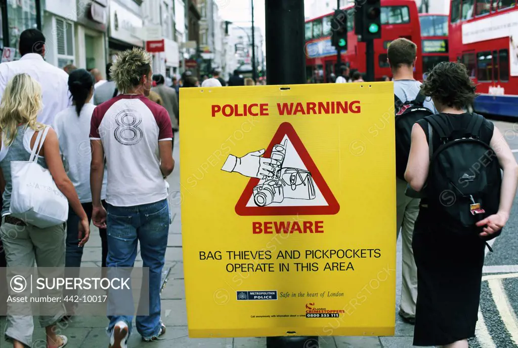 Rear view of a group of people walking near a police warning sign, London, England