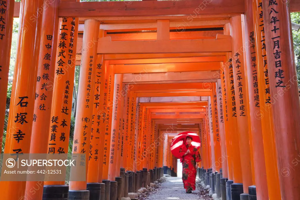 Woman walking in the tunnel of a Torii gate, Fushimi Inari Shrine, Kyoto Prefecture, Kinki Region, Honshu, Japan