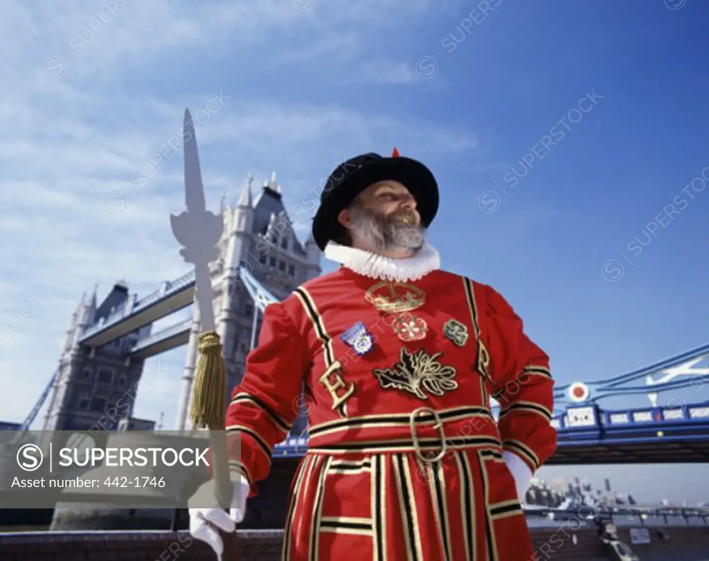 Low angle view of a Beefeater standing with a bridge in the background, Tower Bridge, London, England