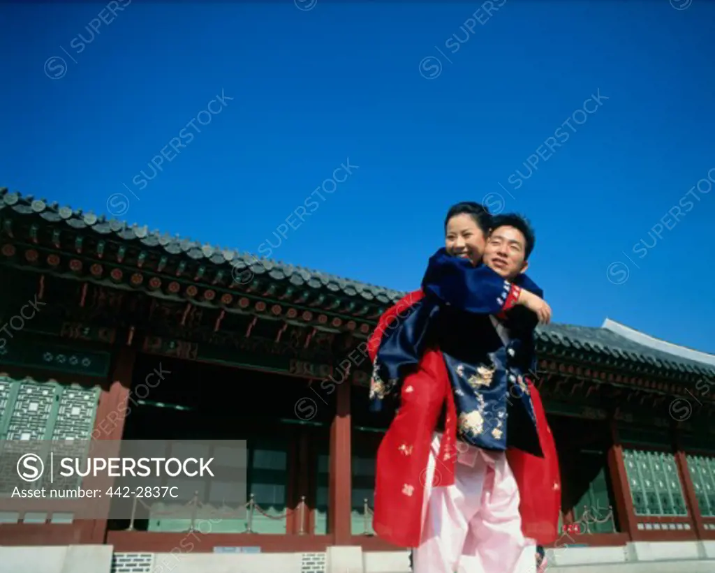 Low angle view of a young woman riding piggyback on a young man, Kyongbok Palace, Seoul, South Korea