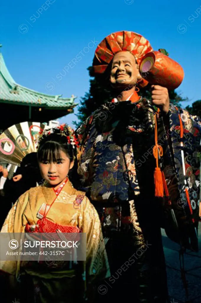 Girl standing in front of a the statue of Daikoku in a festival, Shichi Go San, Tokyo, Japan